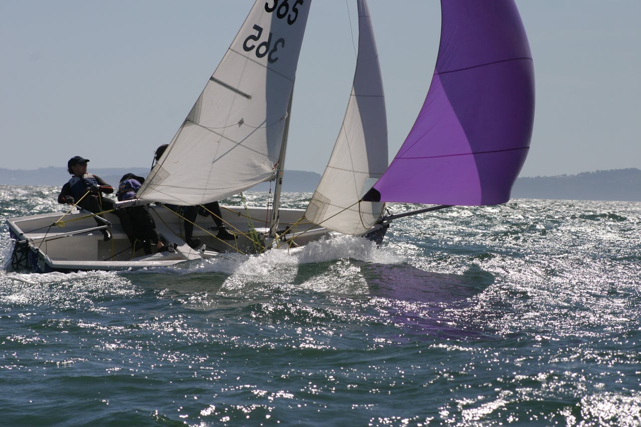 Two sailors navigate a sailboat with colorful spinnaker on a sunny ocean day.